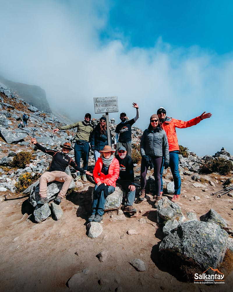 Grupo de sete turistas e seu guia na passagem de Salkantay, ao lado de um cartaz