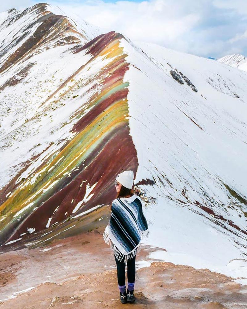 Turista em frente à montanha colorida de Vinicunca, coberta de neve