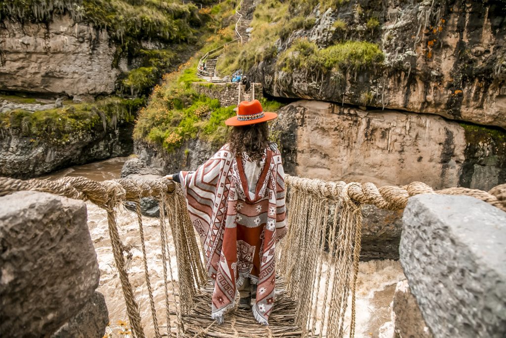Turista com poncho andino na ponte Q'eswachaka