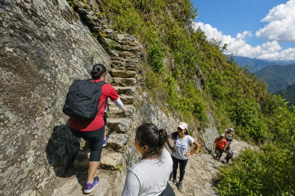 Trilheiros subindo as escadas íngremes de pedra inca cercadas por montanhas verdes exuberantes na Trilha Inca.