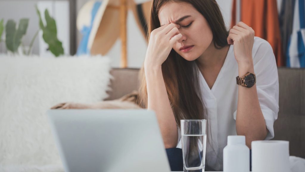 Uma pessoa leva as mãos à testa com uma expressão de dor devido a uma forte dor de cabeça.