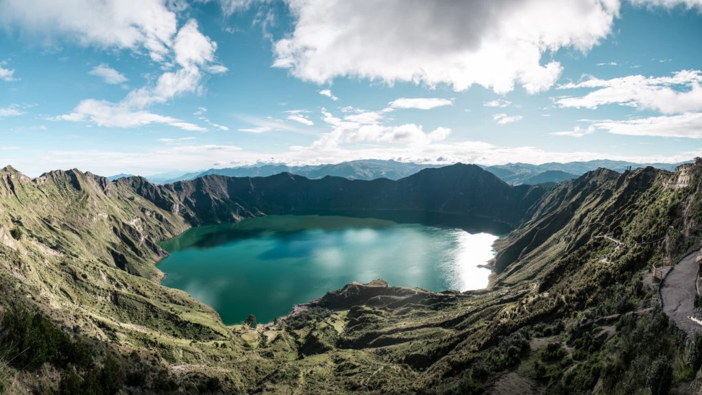 Uma vista panorâmica do enorme lago vulcânico de cor verde-esmeralda da cratera de Quilotoa sob um céu nublado.
