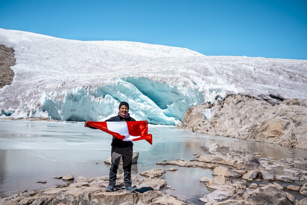 Turista com sua bandeira peruana tendo a geleira Quelccaya ao fundo.