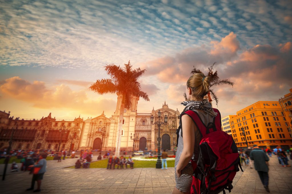 Turista com sua mochila vermelha na praça principal de Lima.