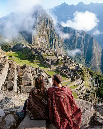 Casal de turistas vestidos com ponchos andinos em frente a Machu Picchu